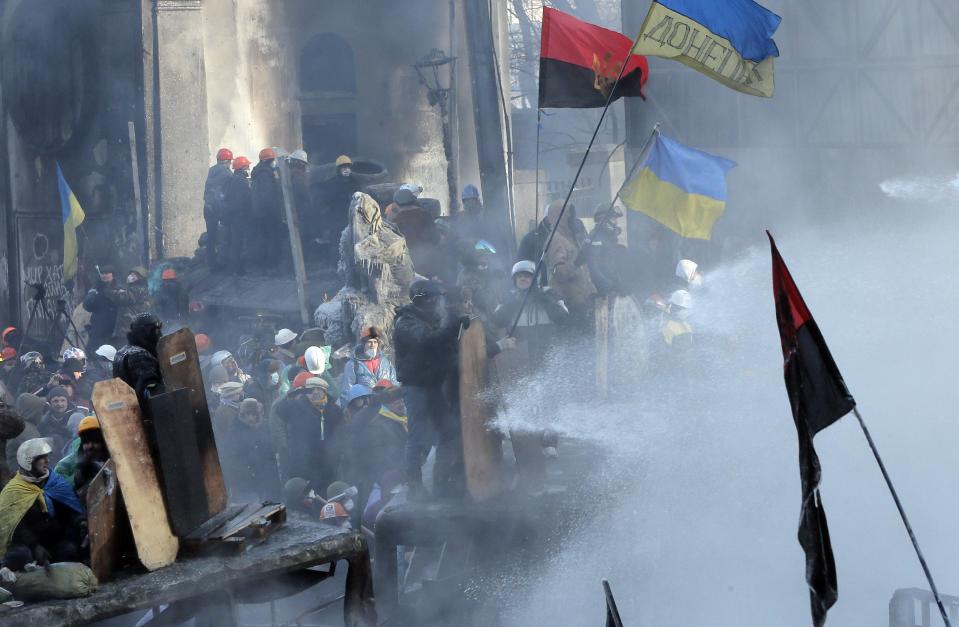 Protesters protect themselves from water guns during a clash with riot police in central Kiev, Ukraine, Saturday Jan. 25, 2014. Ukraine's Interior Ministry has accused protesters in Kiev of capturing two of its officers as violent clashes have resumed in the capital and anti-government riots spread across Ukraine. (AP Photo/Efrem Lukatsky)