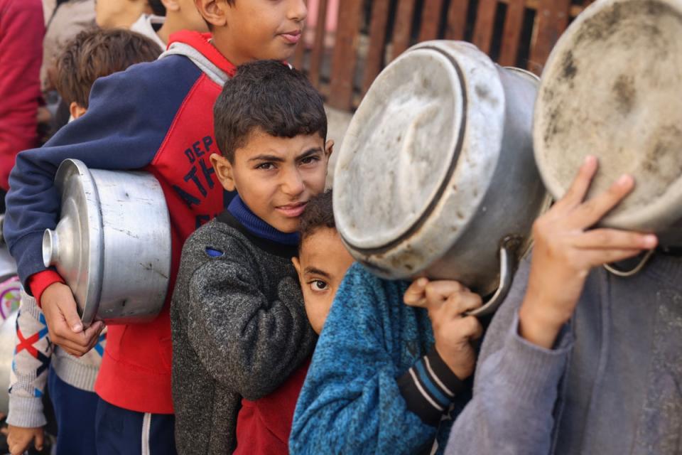 Palestinian children wait to receive food cooked by a charity kitchen in Rafah (Reuters)