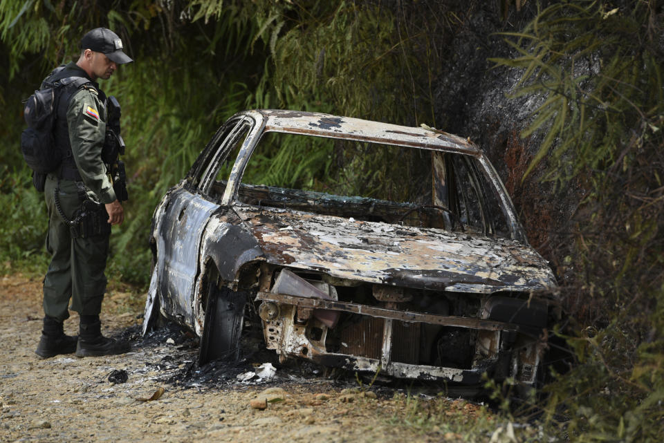 A police officer looks at a vehicle incinerated during a skirmish between illegal armed groups in which at least five people were killed in Jamundi, southwest Colombia, Friday, Jan. 17, 2020. Authorities say rebels with the former Revolutionary Armed Forces of Colombia operate in the area and may have been involved. (AP Photo/Christian EscobarMora)