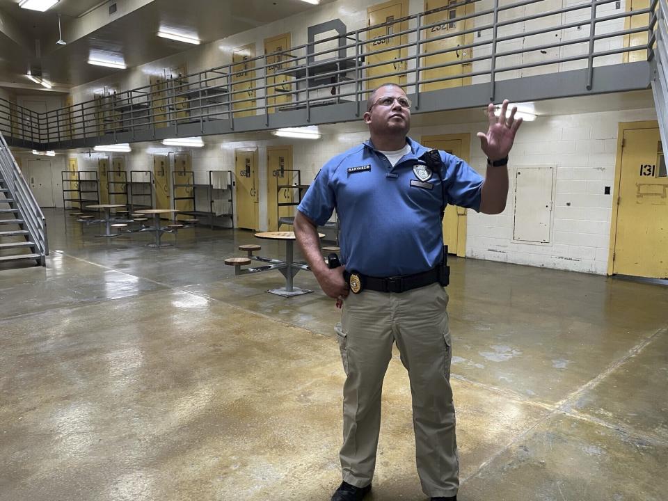 Maj. Albin Narvaez waves to a correctional officer in a secure observation room as he stands in the common area of a prisoner housing unit at the Fulton Reception and Diagnostic Center, Thursday, July 13, 2023, in Fulton, Mo. If the cells are full, prisoners can be placed in the bunk beds in the common area, which can create safety concerns if the prison is short-staffed. (AP Photo/David A. Lieb)