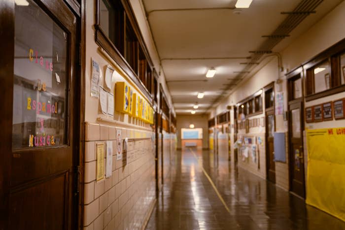 A hallway in a school with various decorations and posters on the walls. The door on the left has a sign in Spanish. The end of the hallway is brightly lit