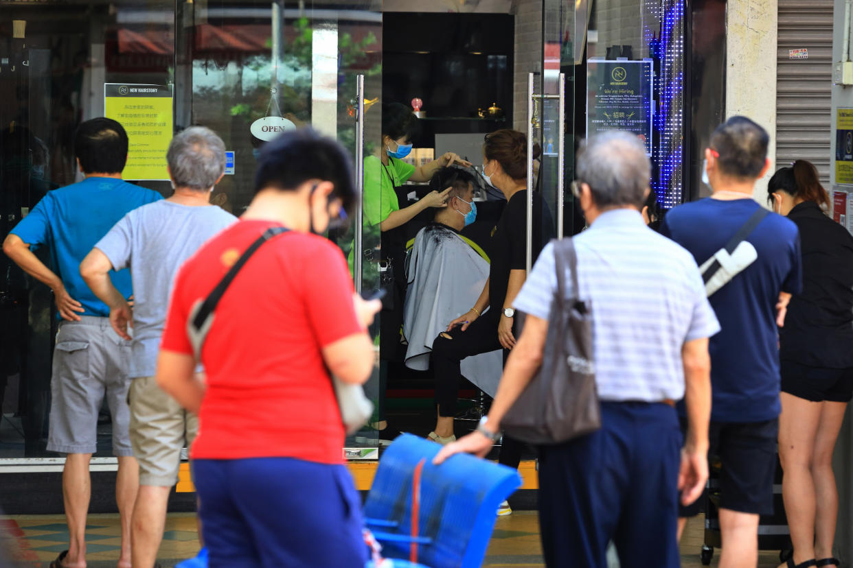 People wearing protective masks wait to enter a hair salon here on 12 May, 2020. (PHOTO: Getty Images)