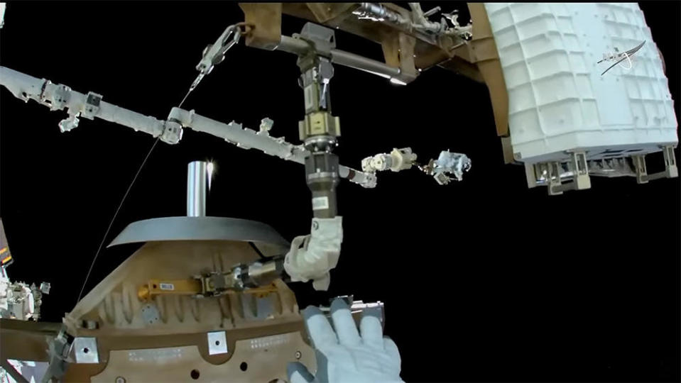 Spacewalker Kayla Barron's helmet camera captures a view of her waving at crewmate Thomas Marshburn, center right, being moved into position to help stow the failed antenna. / Credit: NASA TV