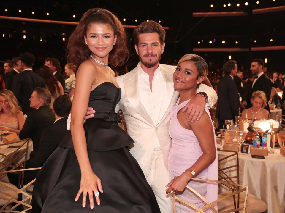 zendaya, in a strapless black dress, andrew garfield, in a cream colored suit, and ariana debose in a pink dress hug each other and pose at the emmy awards
