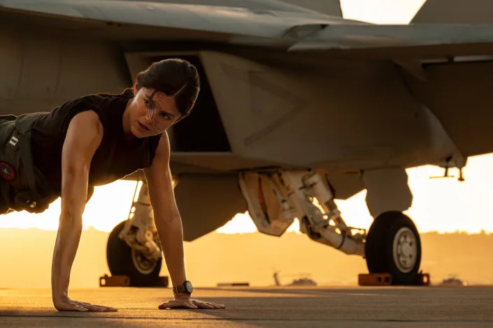 Monica Barbaro doing pushups next to a fighter jet