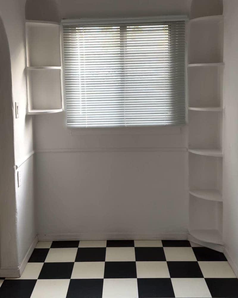 Black and white checkered tile floor, built in book case in corner, blinds on window