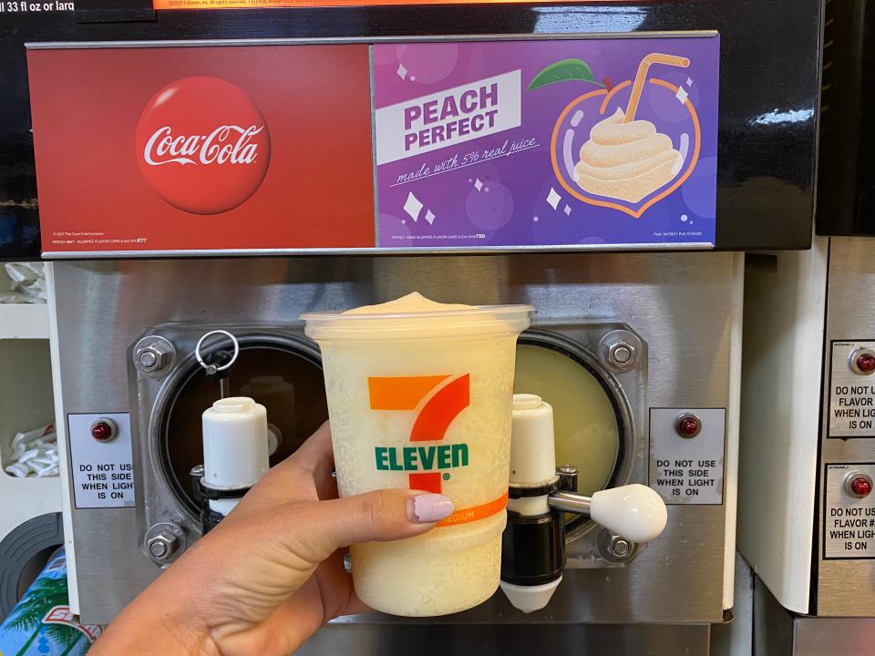 A hand filling up a large 7/11 cup with peach perfect slurpee