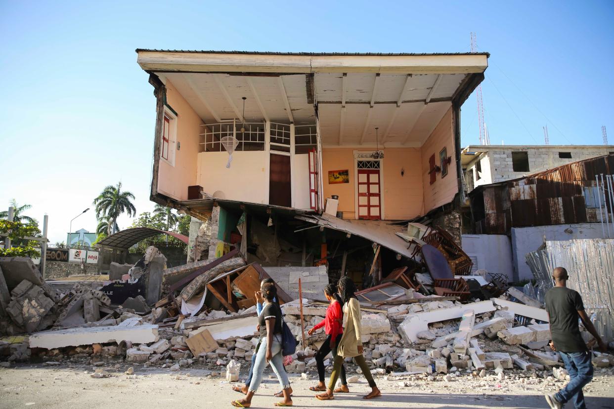 People walk past a home destroyed by the earthquake in Les Cayes, Haiti, Saturday, Aug. 14, 2021.