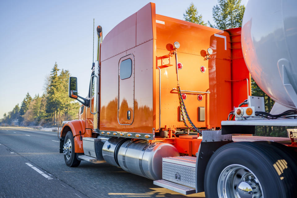 Big orange semi truck hauling a tanker of liquified gas.