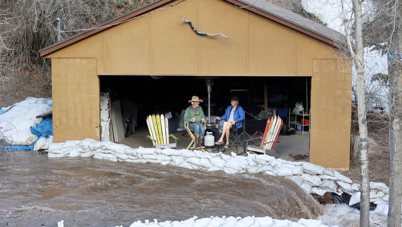 Miguel Jimenez and Andy McNeil chat in McNeil’s garage as water from snowmelt rushes past them on Killyons Lane in Emigration Canyon on Tuesday, May 2, 2023.