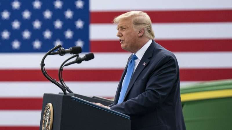 Donald Trump speaking in front of a flag
