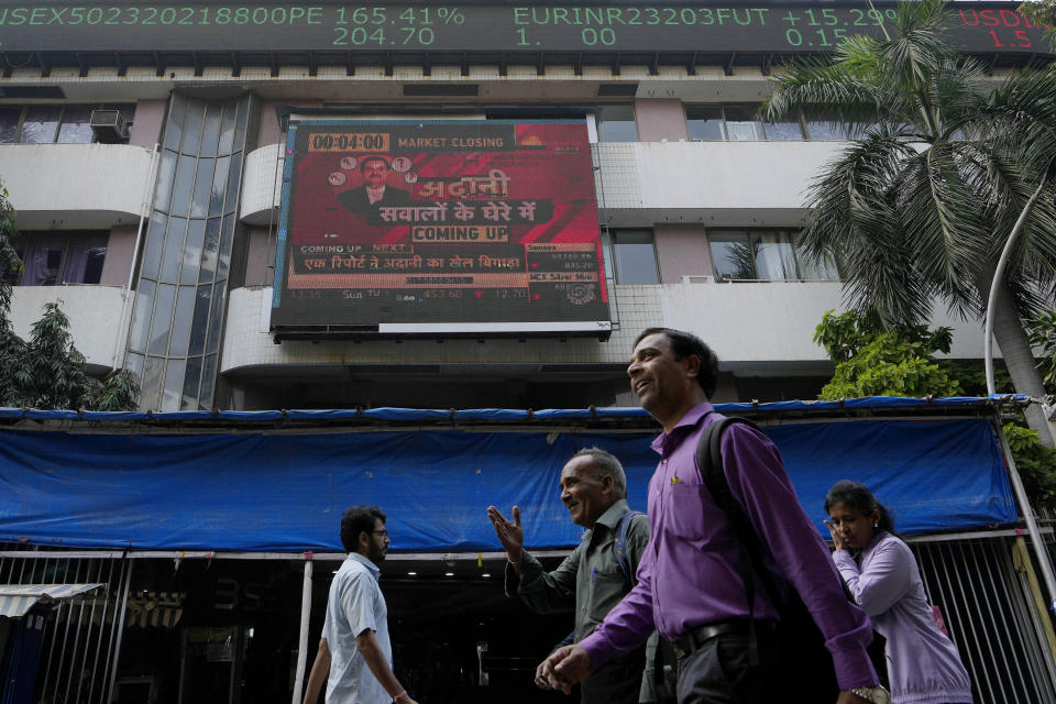 People walk past an electronic display featuring news about Adani Group outside the Bombay Stock Exchange building in Mumbai, India, Friday, Jan. 27, 2023. India’s Adani Group launched a share offering for retail investors Friday as it mulled taking legal action against U.S.-based short-selling firm Hindenburg Research over a report that led investors to dump its shares, with some stocks in the group falling up to 20% on Friday. (AP Photo/Rajanish Kakade)