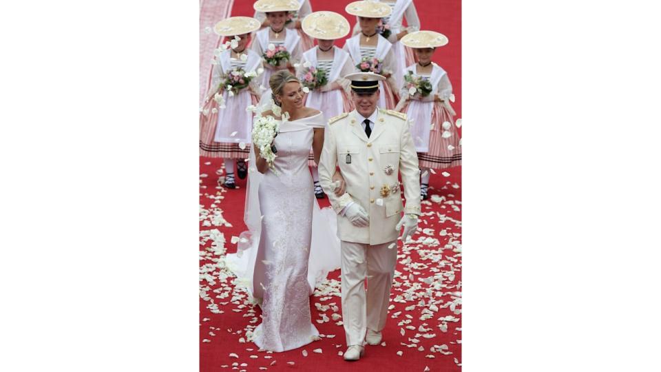 Princess Charlene with her hand through Prince Albert's arm as they're showered with petals following their wedding