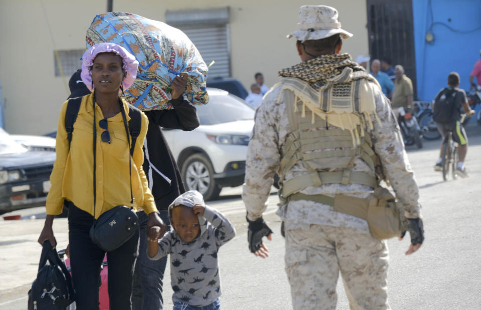 A mother and child walk next to a Dominican Republic security officer on a border bridge between Dajabón, Dominican Republic, and Haiti, Thursday, Sept. 14, 2023. The president of the Dominican Republic announced Thursday that he would close all borders with neighboring Haiti starting Friday in response to the construction of a supposed canal on Haitian soil that targets waters from the Massacre River, which runs along the border shared by both countries. (AP Photo/Ricardo Hernández)