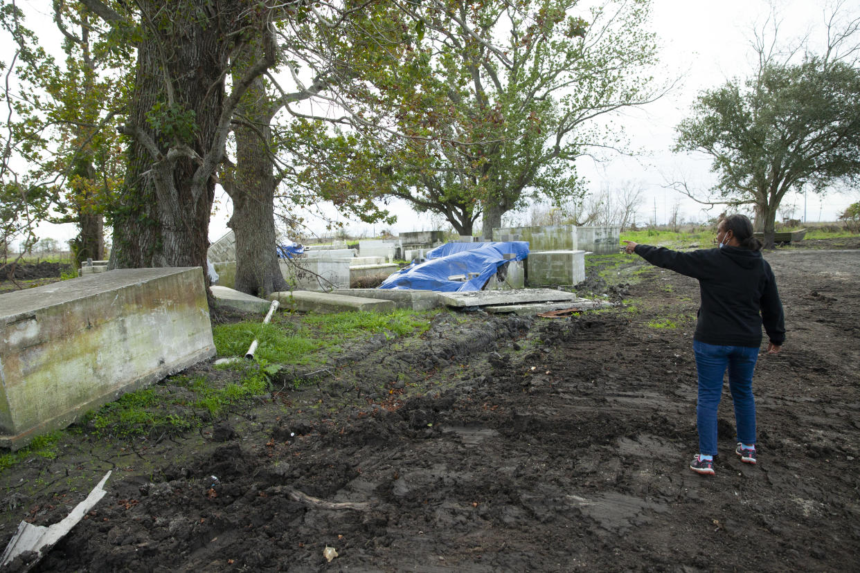 Cassandra Wilson stands on a dirt path and points to stone caskets and lids strewn about beneath trees.