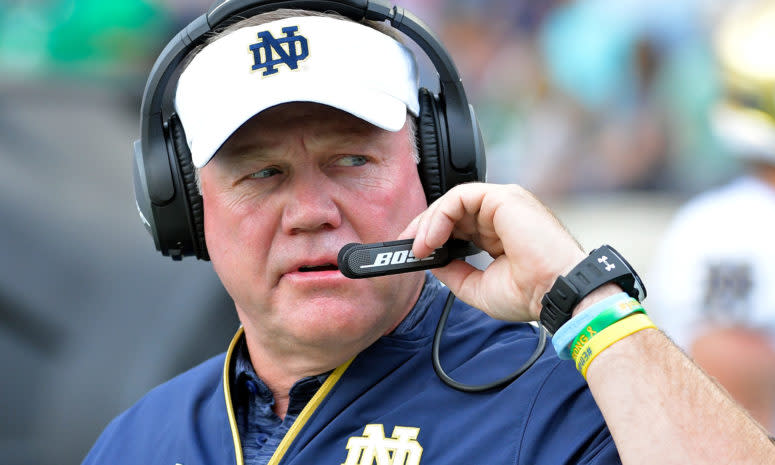 An extreme closeup of Brian Kelly wearing a Notre Dame hat and a head set.