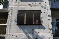 An elderly woman looks out of her apartment window in a damaged building from a May rocket attack in Sloviansk, Donetsk region, eastern Ukraine, Saturday, Aug. 6, 2022. (AP Photo/David Goldman)