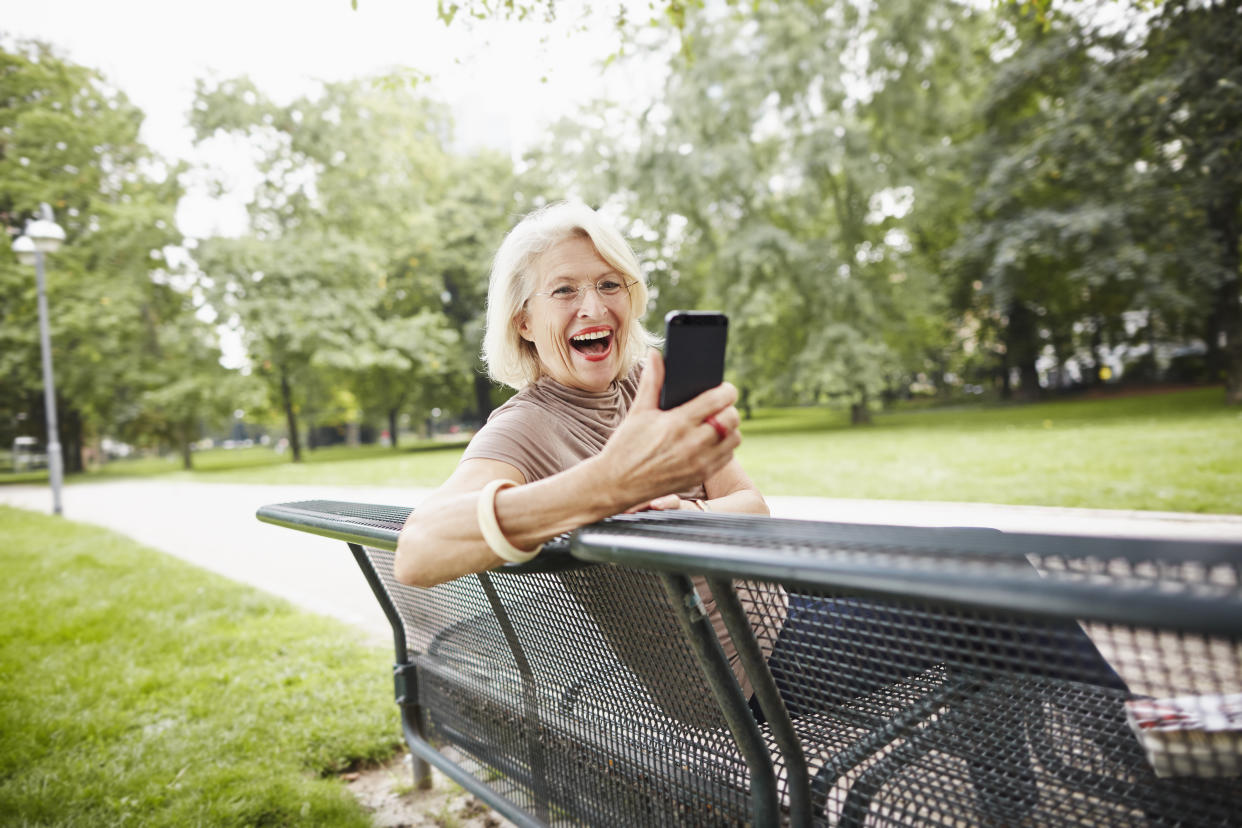 Woman on a bench smiling at a smartphone.