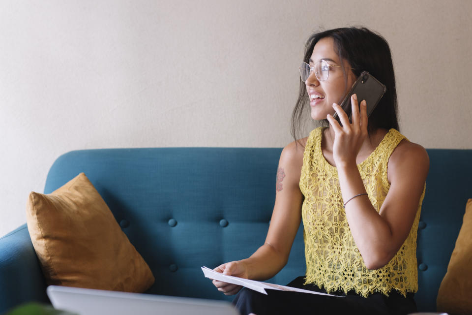 Smiling young woman sitting on couch talking on the phone