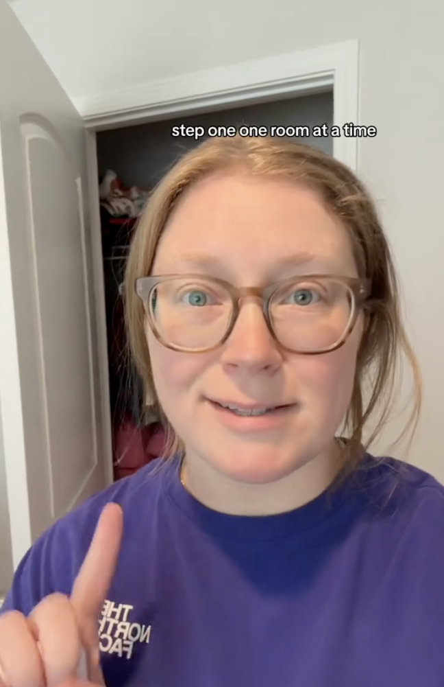 Cindell stands in front of an open cupboard and holds up a finger.