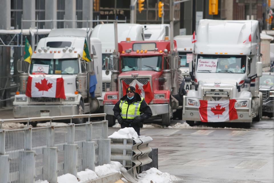 A police officer stands in front of trucks blocking downtown streets as a rally against COVID-19 restrictions, which began as a cross-country convoy protesting a federal vaccine mandate for truckers, continued in Ottawa on Wednesday.