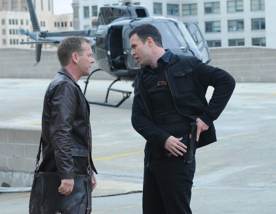 Kiefer Sutherland and Freddie Prinze Jr. in a scene from "24," standing on a rooftop with a helicopter in the background. Sutherland wears a leather jacket