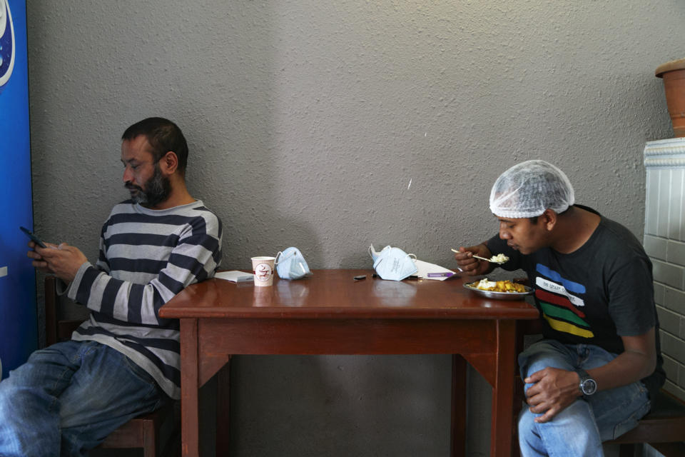 Pharmacist Bikram Bhadel uses his phone as his taxi driver friend Indra Kumar Newar eats his lunch before delivering food at Teaching hospital in Kathmandu, Nepal, Monday, Aug. 31, 2020. At one of the largest hospitals in Nepal, this pharmacist and taxi driver have teamed up to feed COVID-19 patients, doctors, nurses and health workers. Due to lockdowns, the cafeteria and nearby cafes have closed, leaving more than 200 staffers, patients and their families without food. The two friends have taken their own money and donations and put it to use buying groceries, renting a kitchen and paying helpers to provide the meals. (AP Photo/Niranjan Shrestha)