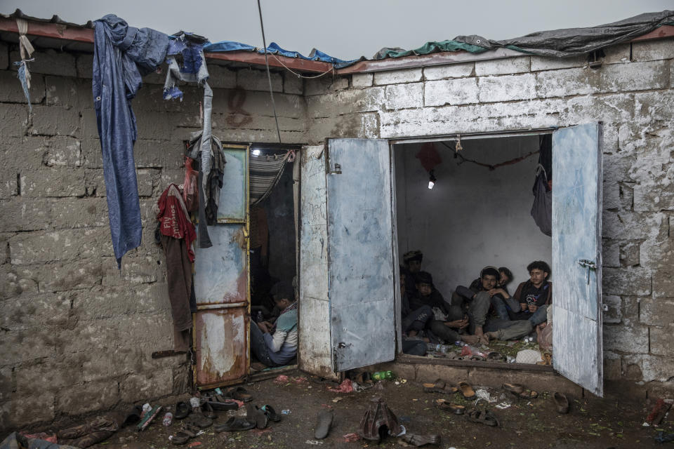 In this Aug. 4, 2019 photo, Yemenis, right, chew qat, while Ethiopian migrants, left, take shelter in a small shack at a qat market in Dhale province in Yemen. This is one of the stops where migrants take shelter to continue their journey to Saudi Arabia, and an active frontline between militiamen backed by the Saudi-led coalition and Houthi rebels only a few hundred meters (yards) away (AP Photo/Nariman El-Mofty)