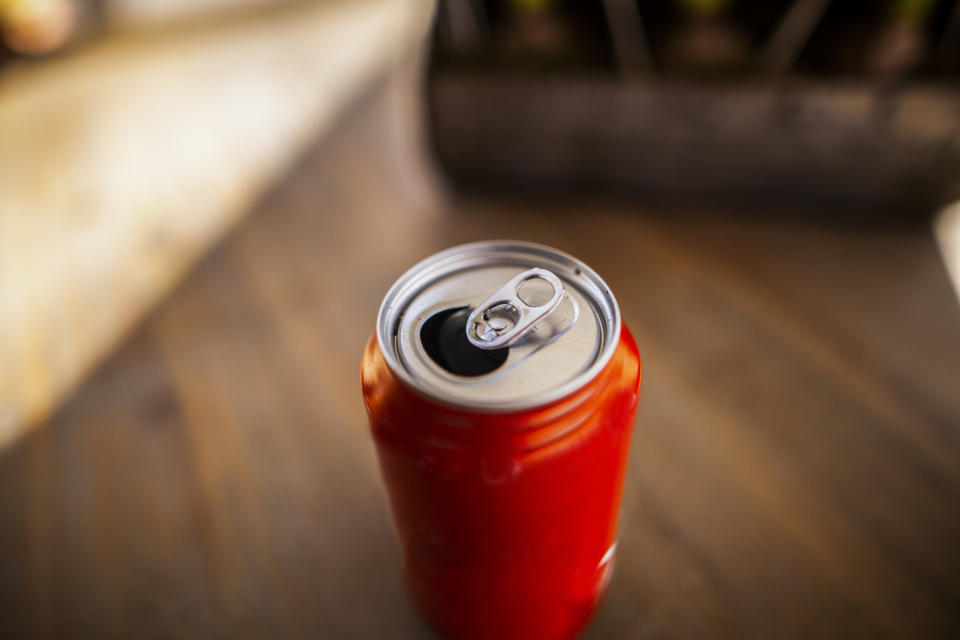 An open soda can on a wooden table, viewed from above