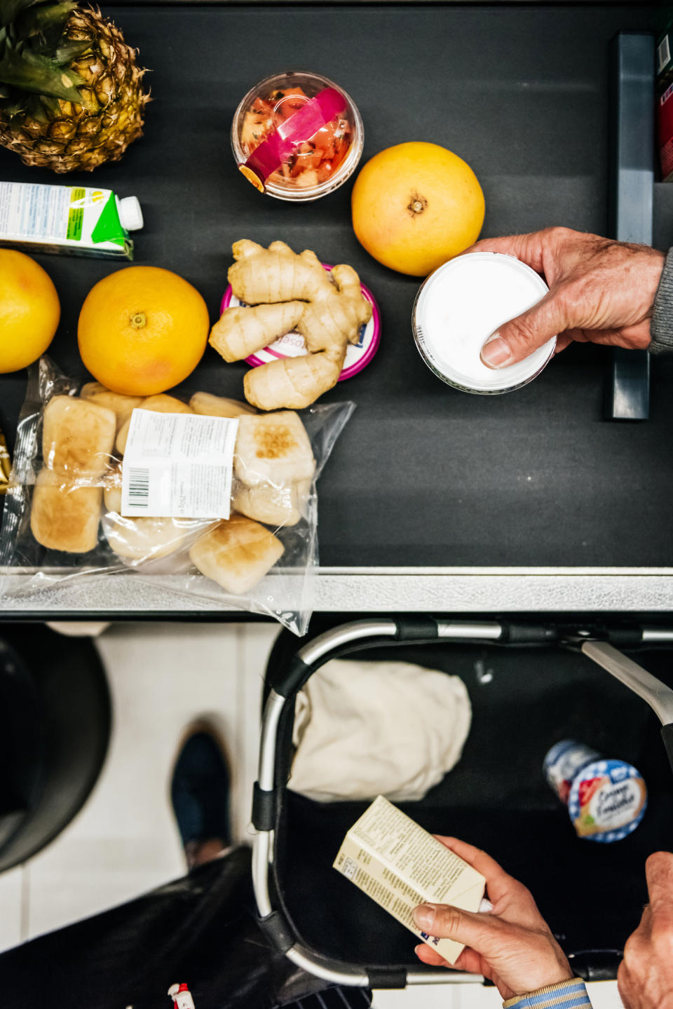 Person unpacking groceries including fruit, yogurt, and ginger onto a kitchen counter