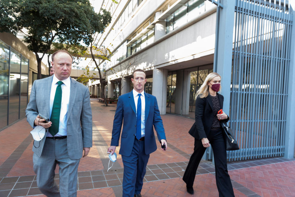 Meta Platforms Chief Executive Mark Zuckerberg, in blue suit and tie, is flanked on a tiled walkway by a man in a gray suit and green tie and a woman in a black pantsuit.