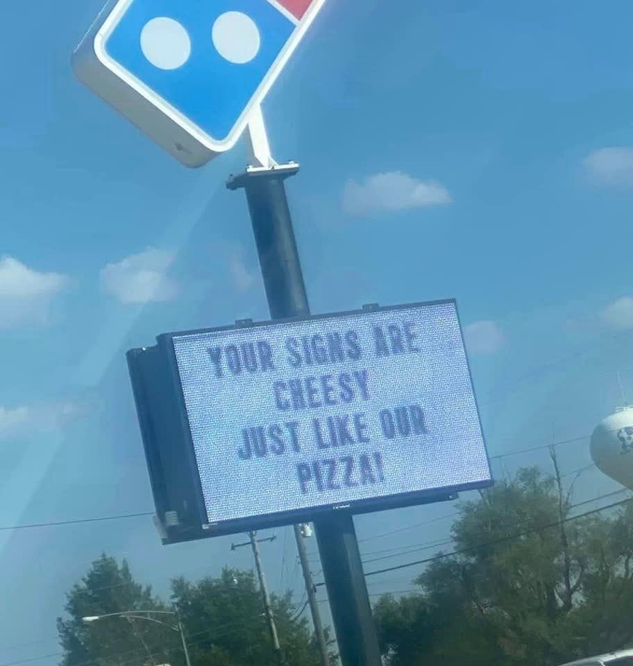 a Domino's sign that says "your signs are cheesy just like our pizza!"