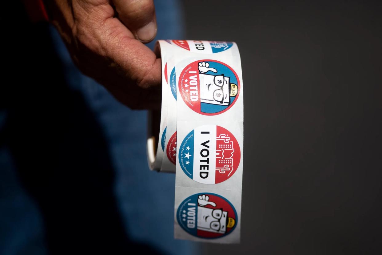 Gene Godwin, an elections worker, holds a roll of stickers for people who vote by dropping their ballots off at the Maricopa County Elections office at 510 S. Third Ave. in Phoenix on Oct. 16, 2020.