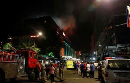 Evacuated employees and guests of hotels stand along a road and watch as smoke billows from a Resorts World building in Pasay City, Metro Manila, Philippines June 2, 2017. REUTERS/Erik De Castro