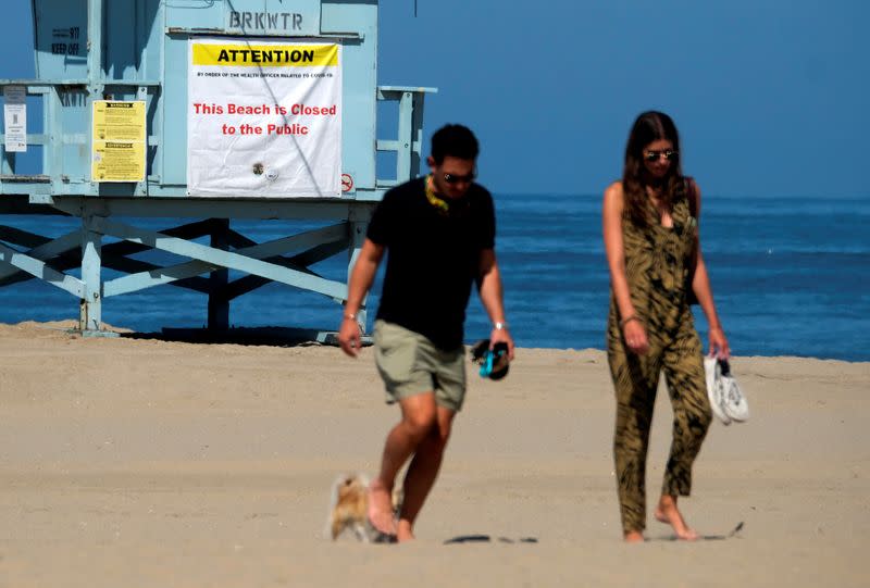 FILE PHOTO: People walk past a beach closed sign hanging on a lifeguard booth during the outbreak of the coronavirus disease (COVID-19) at Venice Beach in Los Angeles