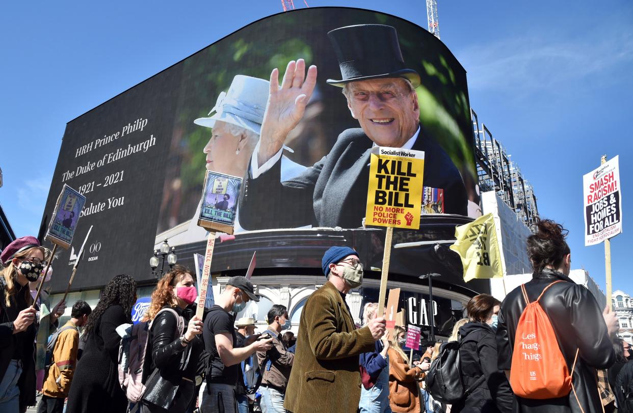 <p>Protesters walk past images of Britain's Prince Philip displayed on a giant screen at Piccadilly Circus</p> (AP)