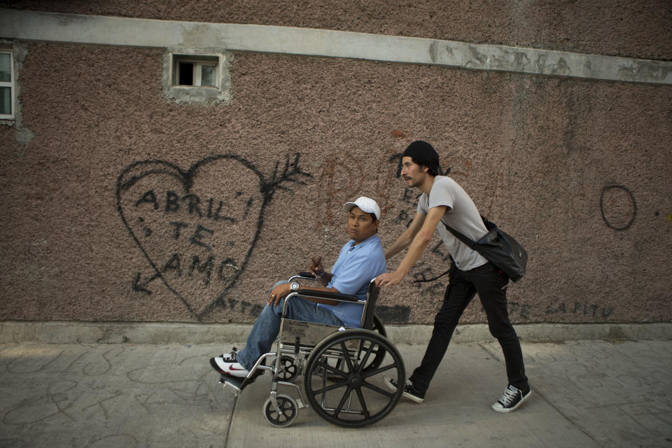 In this April 11, 2014 photo, Martin Camarillo, 35, who was paralyzed by a bullet when he was 19, calls out greetings to neighbors as he and actor Raul Briones lead visitors on a tour of his neighborhood in Tepito, Mexico City. As part of the "Safari in Tepito" theater project, Camarillo welcomes the audience into his bedroom, barely big enough for his bunk bed, and exchanges thoughts with Briones about fatherhood. Camarillo talks about having to accept that he can never have a child and talked about his own father’s alcoholism, womanizing and domestic abuse. (AP Photo/Rebecca Blackwell)