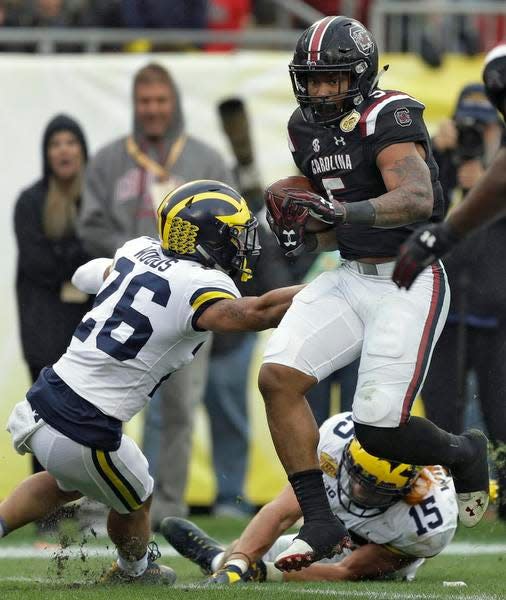 South Carolina running back Rico Dowdle (5) runs over Michigan defensive back J'Marick Woods (26) and defensive lineman Chase Winovich (15) on the way to an 18-yard touchdown during the second half of the Outback Bowl.