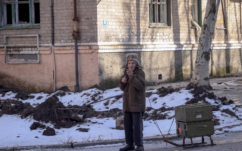 A local resident rests as he walks with empty ammunition boxes on a street in the front line city of Bakhmut - STRINGER/REUTERS