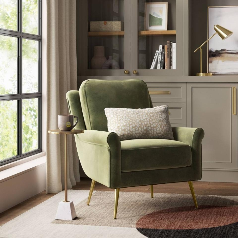 A green velvet armchair with a white pillow in a stylish room setting