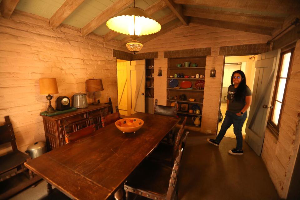 A woman stands in a whitewashed room with a long table.