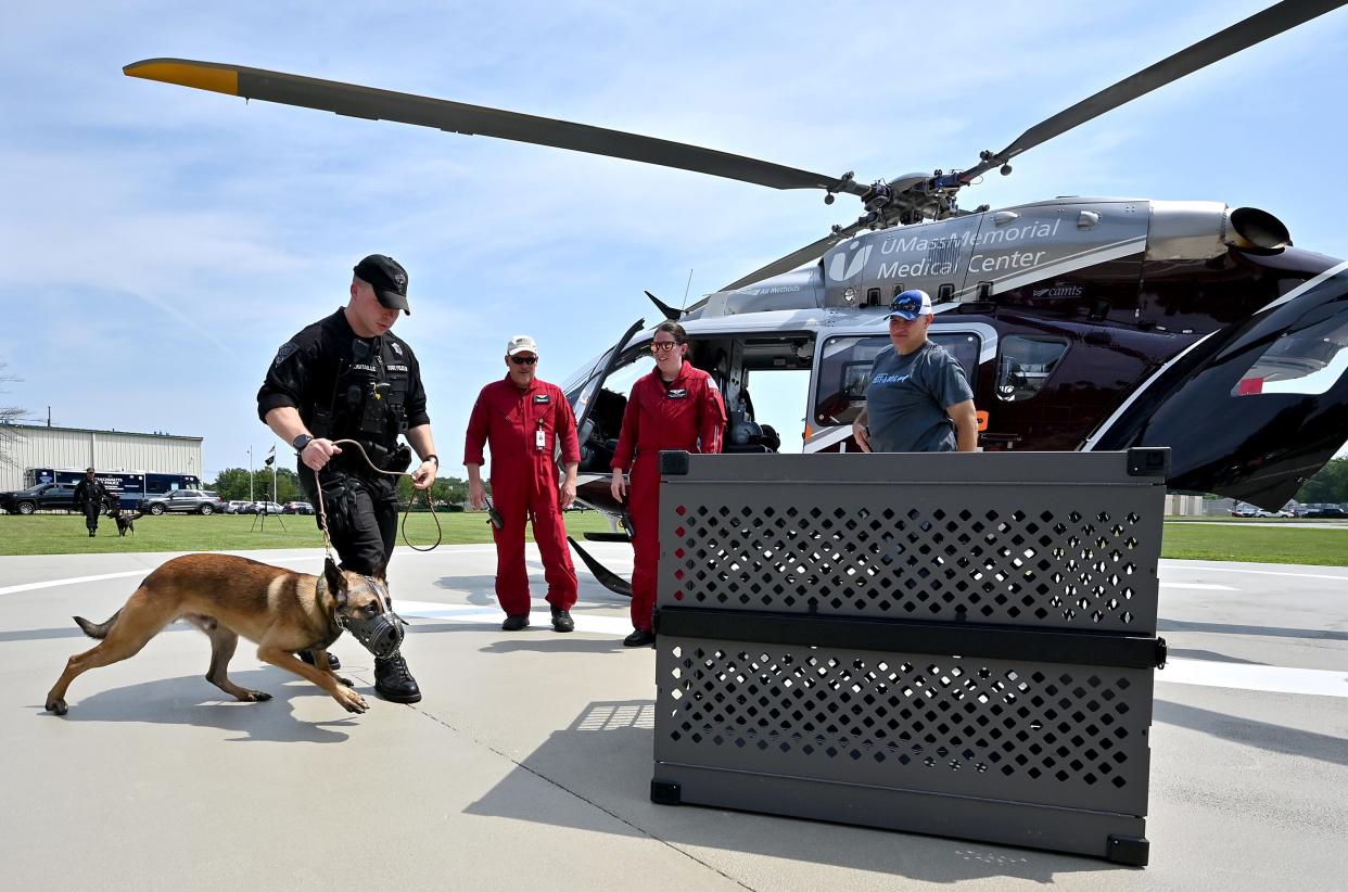 Mass. State Trooper Nathan Robitaille guides his K-9 police dog Bosco to a cage which will be loaded into a UMass LifeFlight as part of a helicopter landing and K-9 air medical transport training exercise at Massachusetts State Police headquarters. Watching are, from left, LifeFlight crewmembers EMT/paramedic Glenn Olson of North Smithfield, R.I., and flight nurse Stacy Cicio of Charlton, as well as Dave Shilale of Massachusetts Vest-a-Dog.