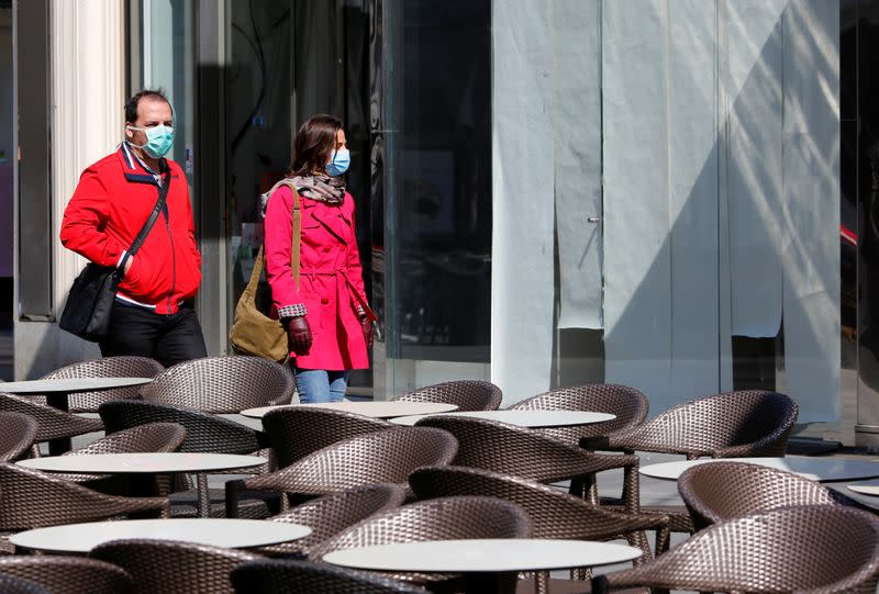 People wearing protective face masks pass closed shops in Vienna