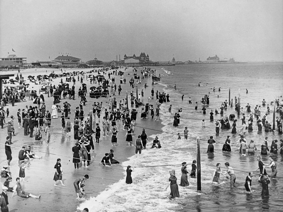 People swim in the ocean and sit on the beach at Coney Island in 1898.