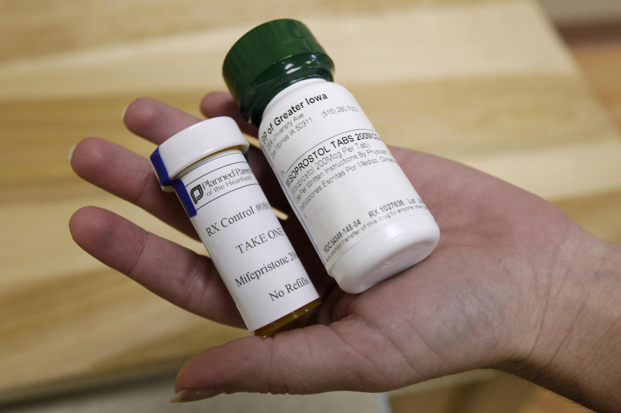 An outstretched hand holds bottles of mifepristone and misoprostol at a clinic.