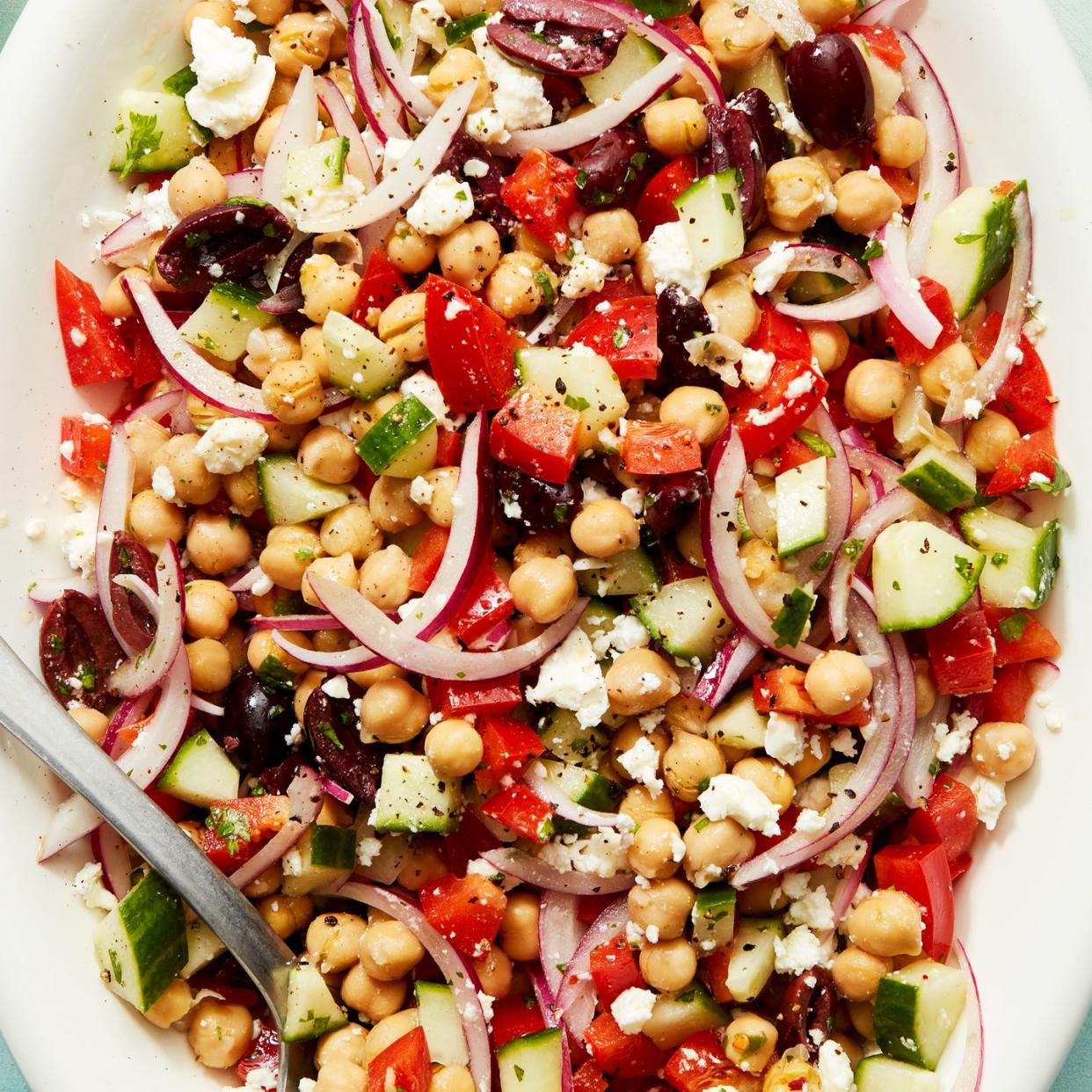 Chickpeas, olives, feta cheese, cucumber, sliced ​​red onion and red bell peppers served on a white plate