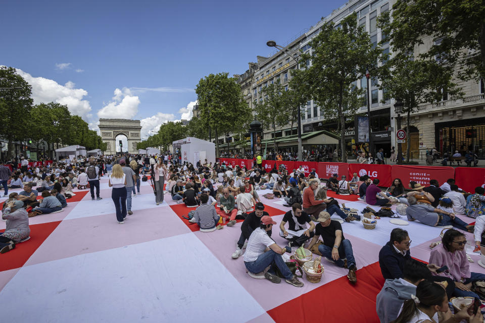 People eat their lunches as part of a giant picnic on the Champs-Elysées, in front of the Arc de Triomphe, organized by the Comité Champs-Élysées, Sunday, May 26, 2024 in Paris. (AP Photo/Aurelien Morissard)