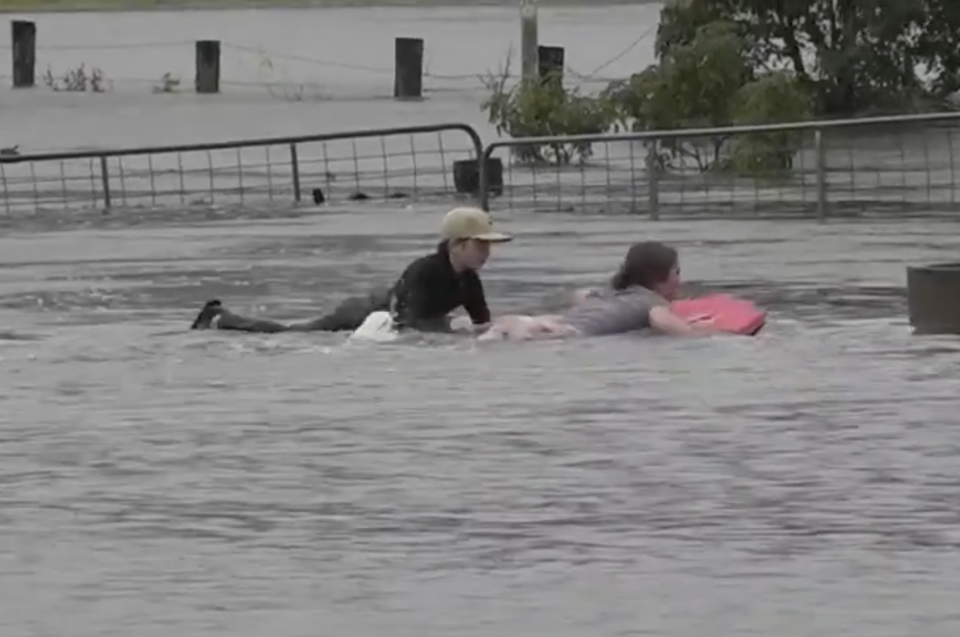 Two children use bodyboards to navigate a flooded property in NSW.