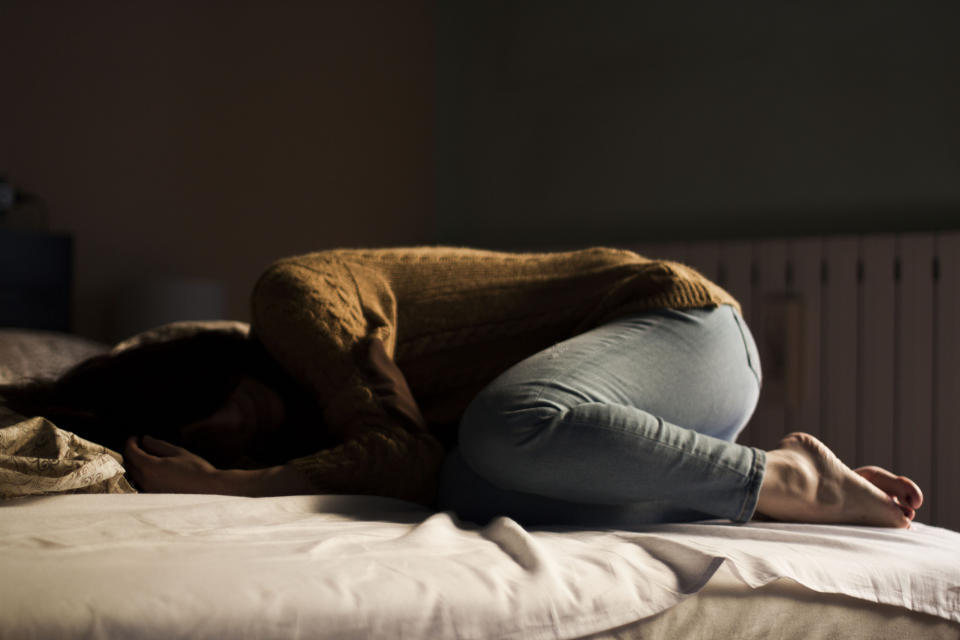 A woman with depression curls up in bed. 