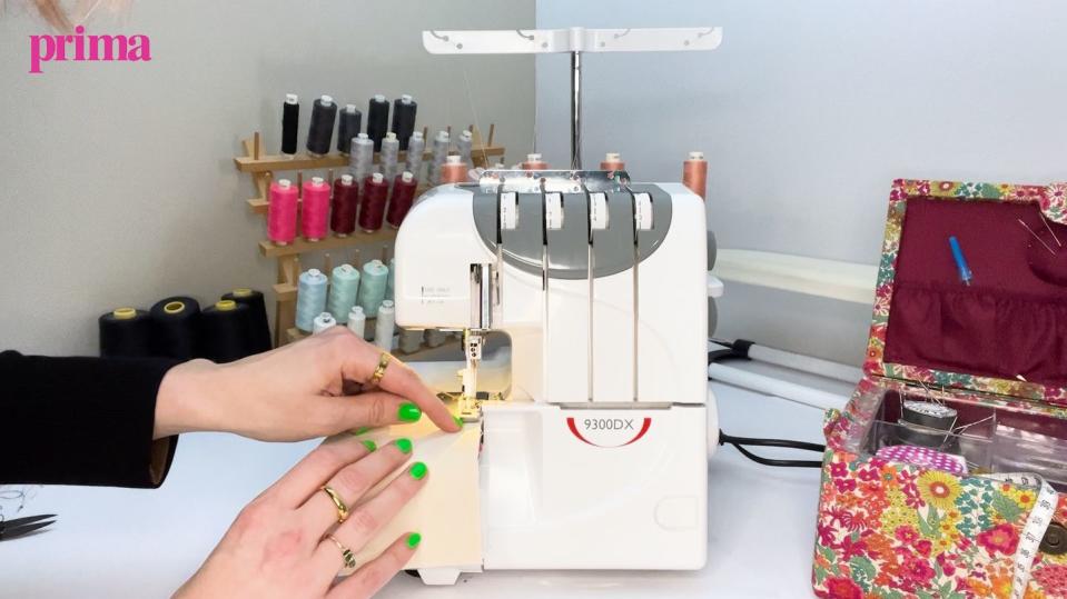 womans hands holding fabric under an overlocker sewing machine